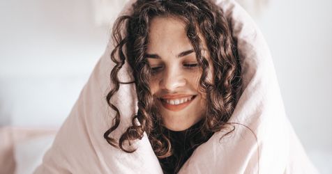 smiling woman wrapped in gray blanket to care for self