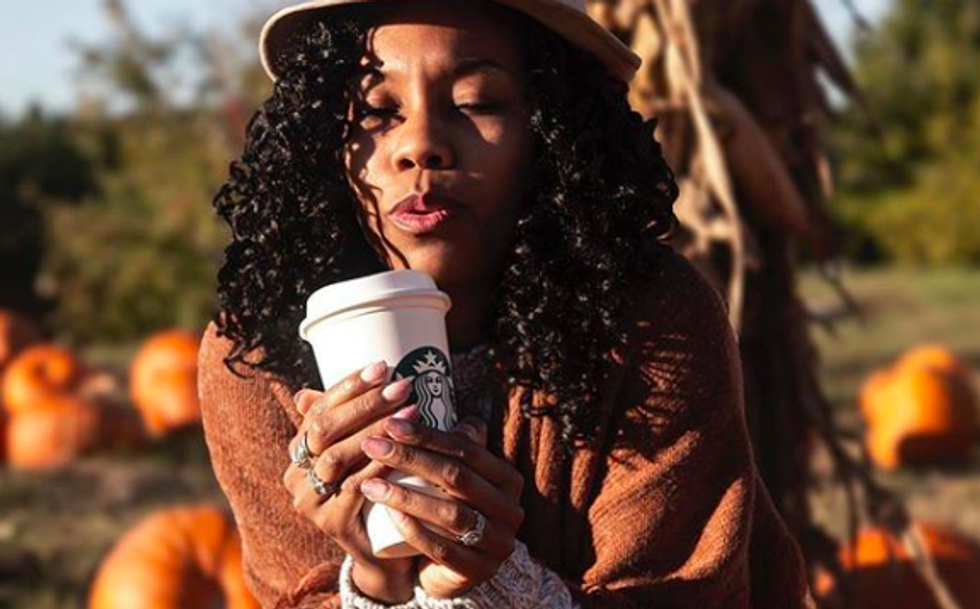 someone in sweater holding a Starbucks mug in front of a pumpkin patch