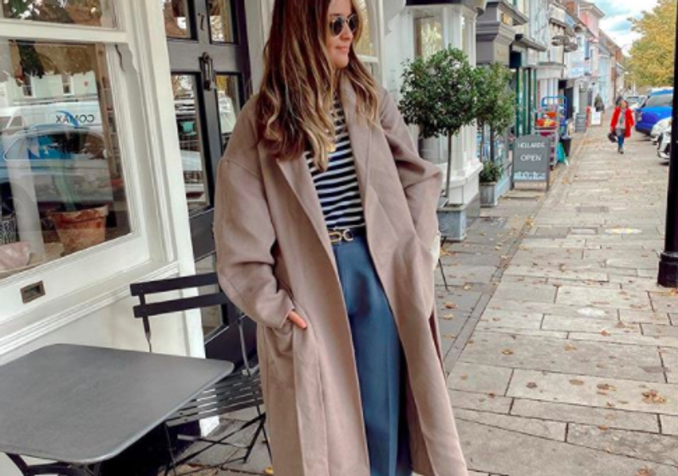 someone standing outside wearing a tan coat, sunglasses, striped shirt, and blue baggy pants