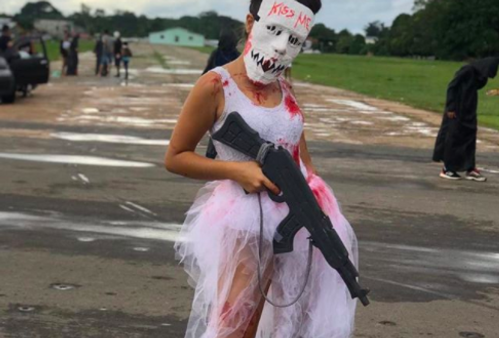 someone wearing white tulle skirt and white tank with blood on it holding a gun and wearing a mask that says "kiss me" on it