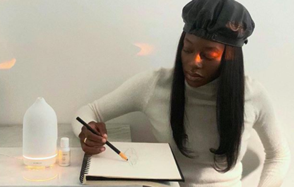 stylish person sketching in a notepad with an oil diffuser next to them