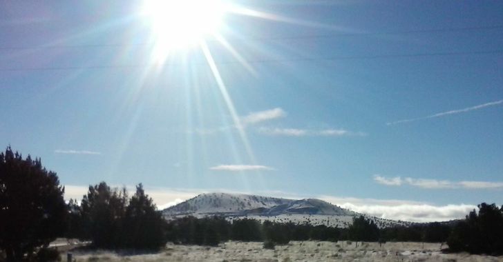 Sun shining over a cinder hill covered in a dusting of snow