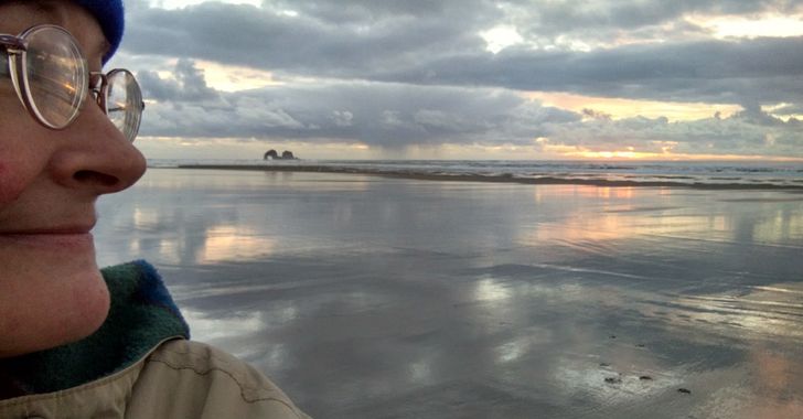 The author's profile in front of a sunset on Rockaway Beach in Oregon with sunset reflecting off of a wet beach