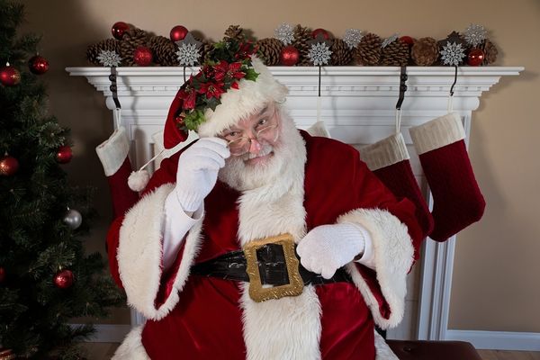 The character Santa Claus sitting in front of a fireplace and Christmas tree.