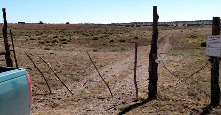The corner of a green pickup tailgate in front of a cowboy fence of barbed wire and sticks