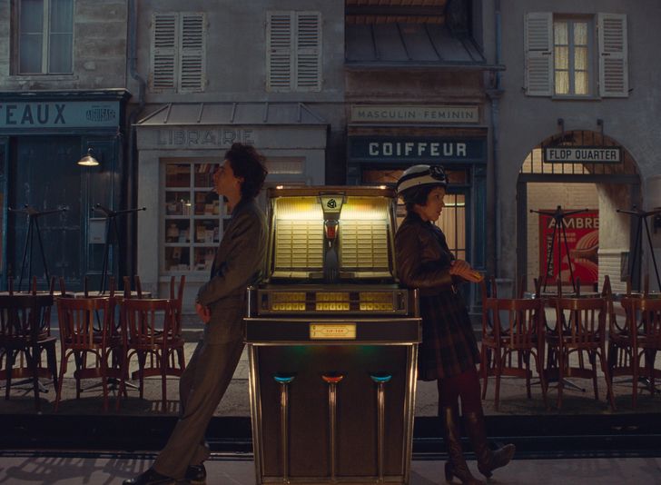 Timothée Chalamet and Lyna Khoudri stand on opposite sides of a vintage jukebox, backs to each other in a movie still from "The French Dispatch."