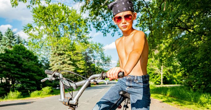 topless boy in blue denim jeans riding red bicycle during daytime