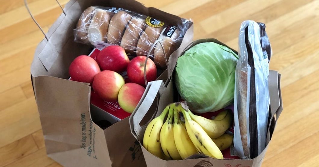 two large brown bags filled with apples, bagels, bananas, lettuce, frozen pizzas, etc.
