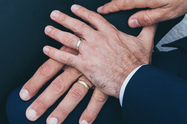 two men hold hands with rings reflecting gay marriage
