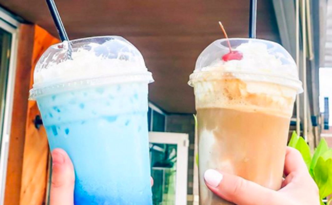 two people holding up cups with a blue and brown drink, both with ice cream on top