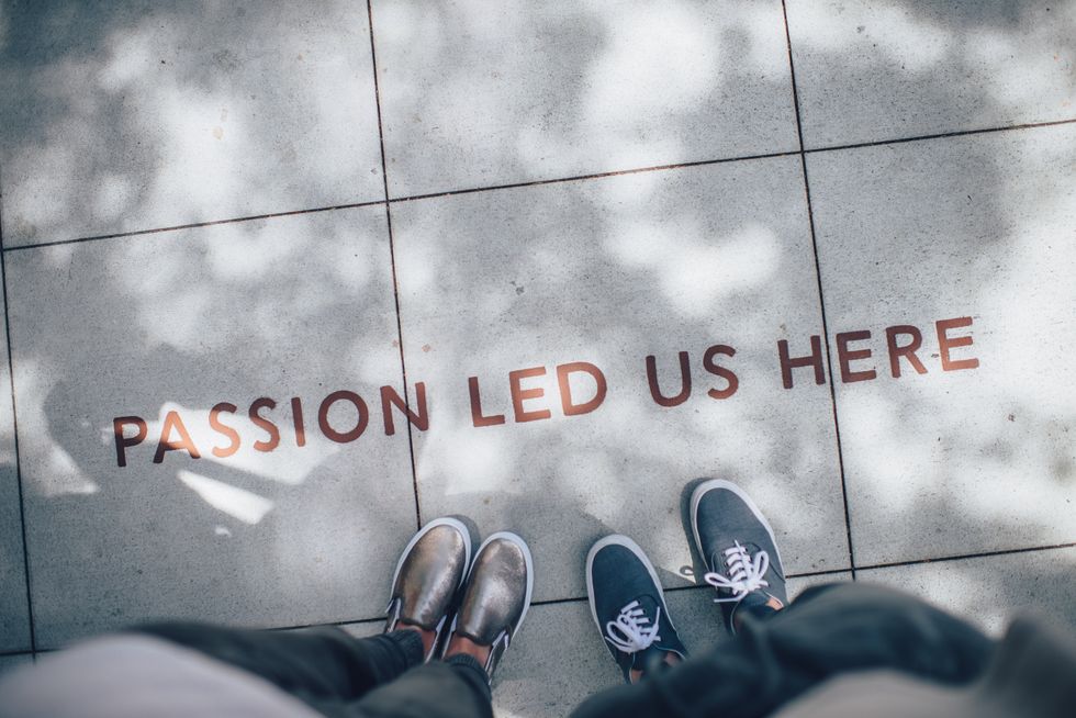Two person standing on gray tile paving that says 'Passion Led Us Here' written.