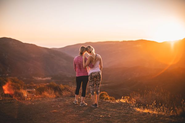 two women standing on moutain half-hugging each other