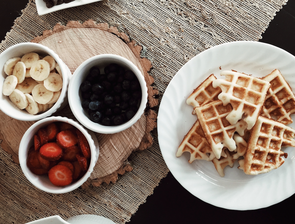 waffles beside bowls of strawberries, banana, and black berries