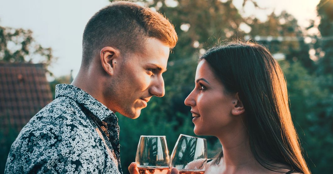 Woman and man face to face Interlocking wine glasses and smiling at eachother 