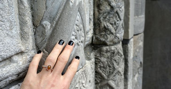 Woman holding concrete wall in black nails