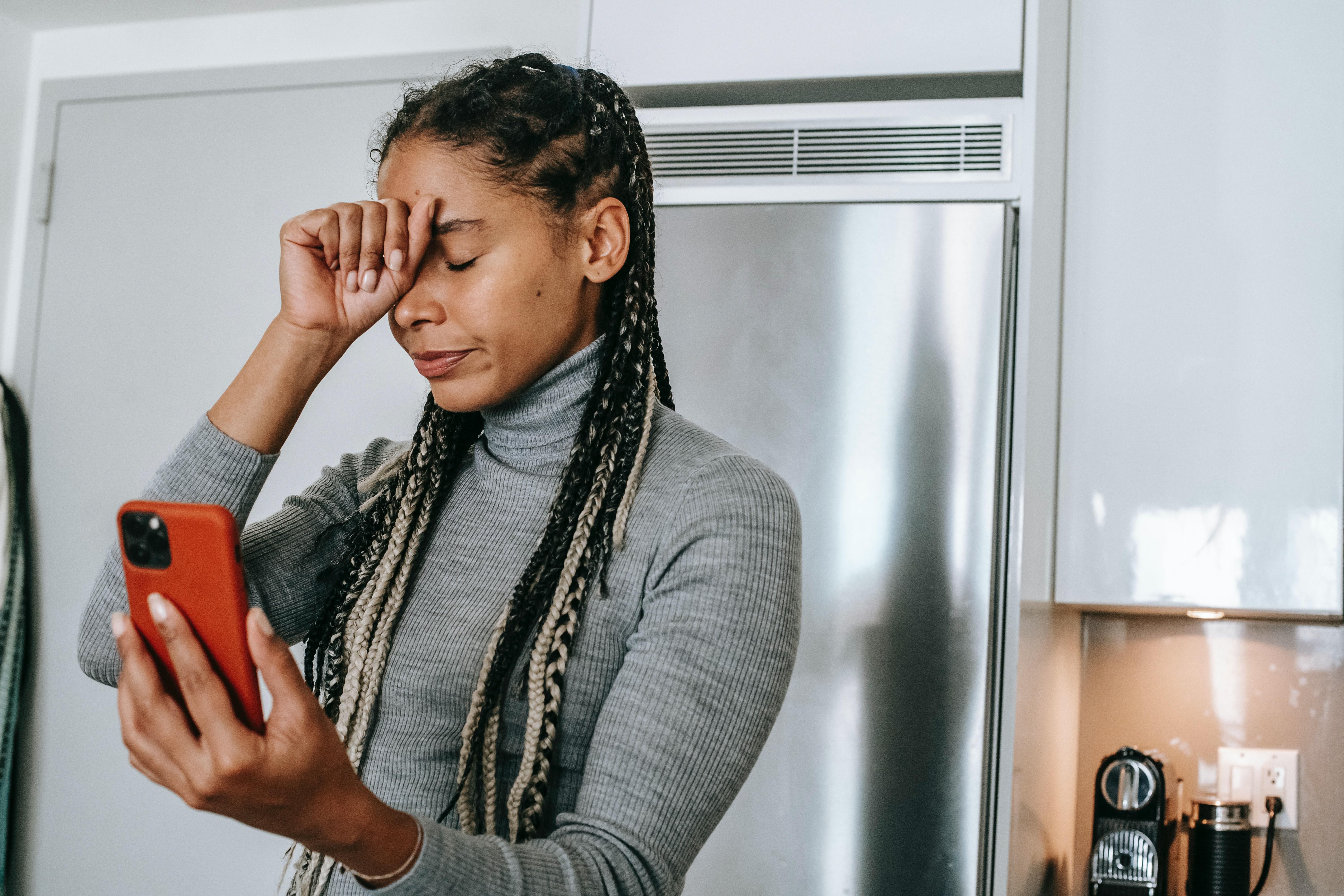 Woman holding her phone in one hand and head in the other hand.
