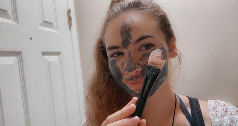 Woman holds liquid applicator with charcoal mask on face.