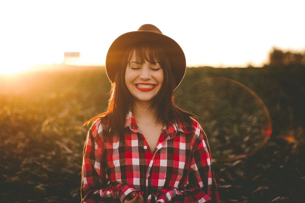 woman in had and checkered flannel smiling in field