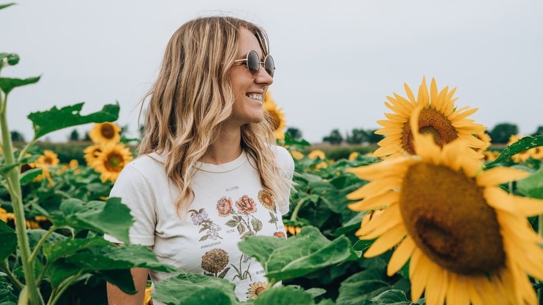 woman in sunglasses smiling in field of sunflowers
