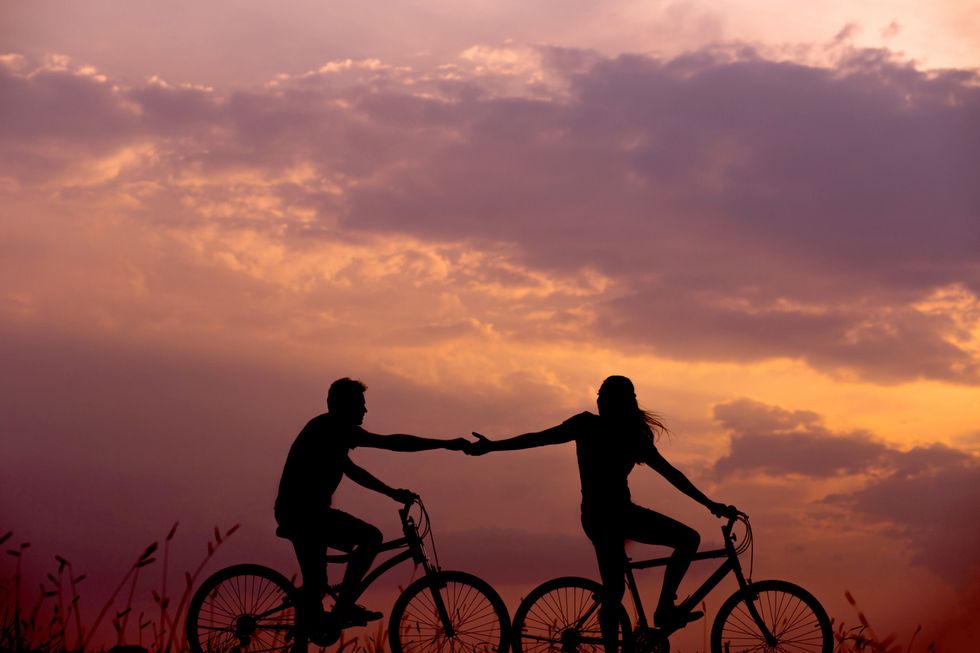 Woman on bike reaching out for a man on a bike in front of a sunset