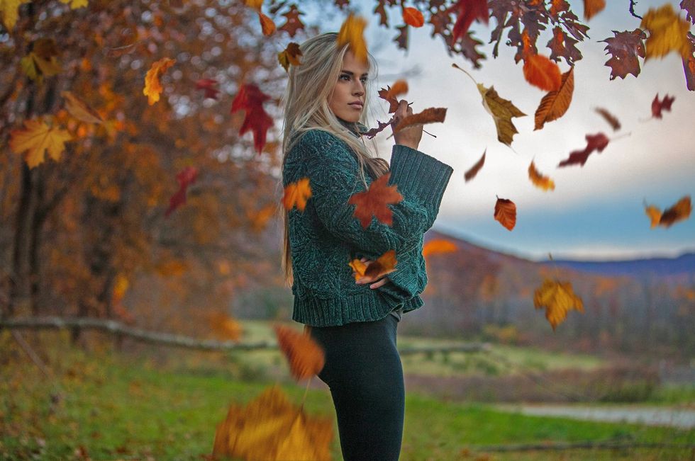 Woman posing candidly underneath a tree while autumn leaves fall midair 
