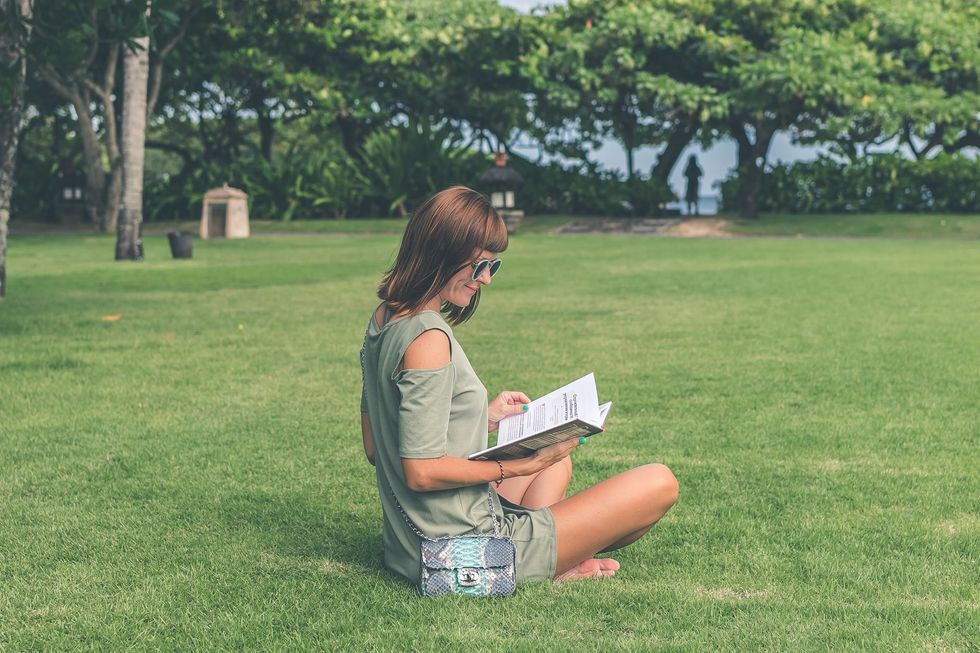 Woman sitting down and reading a book in a grassy area
