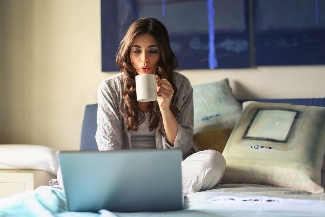 woman sitting in bed on laptop drinking coffee