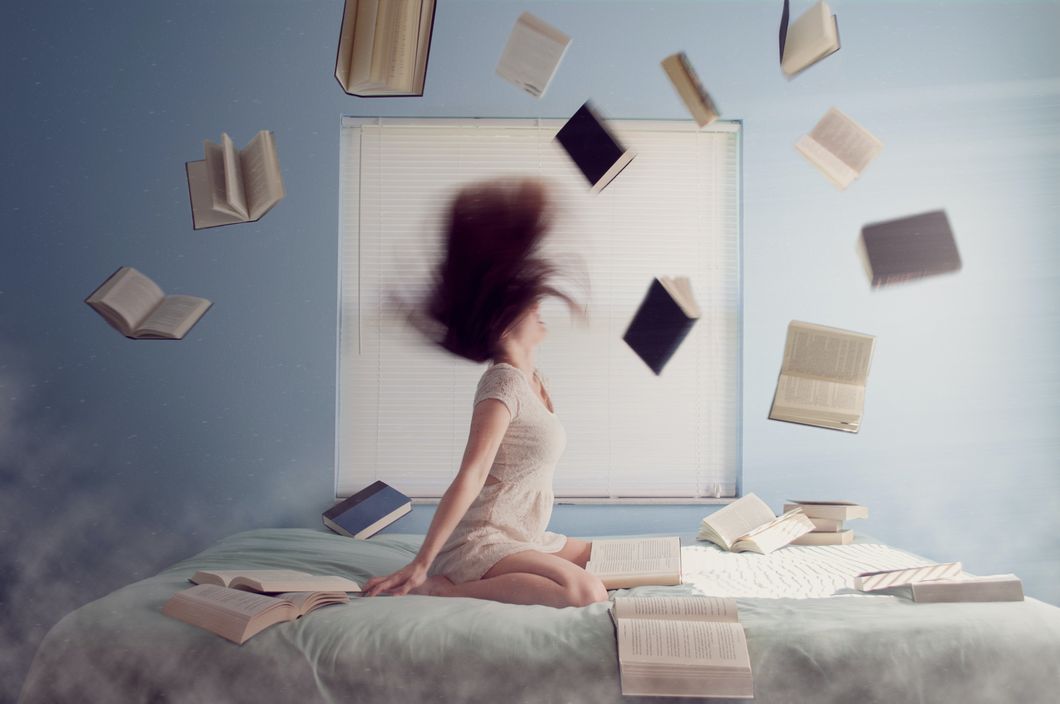 Woman sitting on her bed with books all around her.