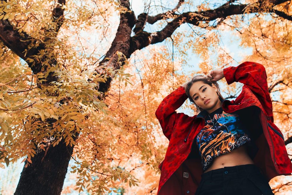 Woman underneath a tree with fall-colored leaves, looking down at camera