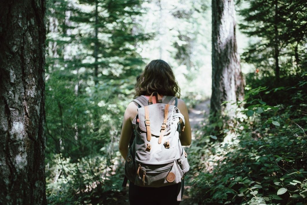 woman walking through forest with backpack