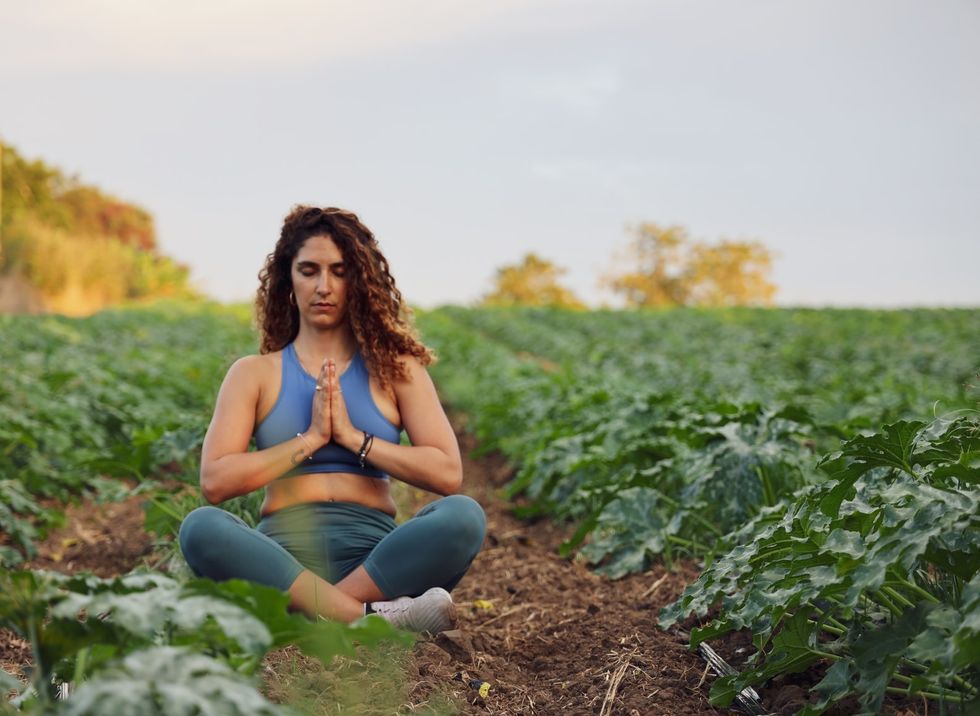 woman wearing blue sports bra and leggings sitting in a field with hands at her heart
