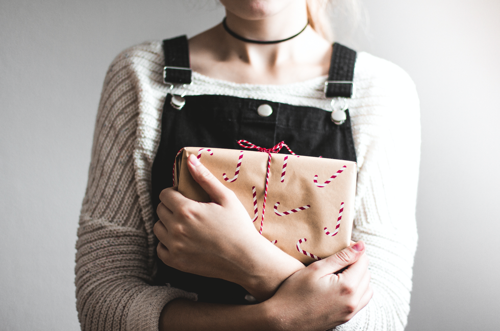 woman wearing grey sweater and black overall pants while holding brown bag