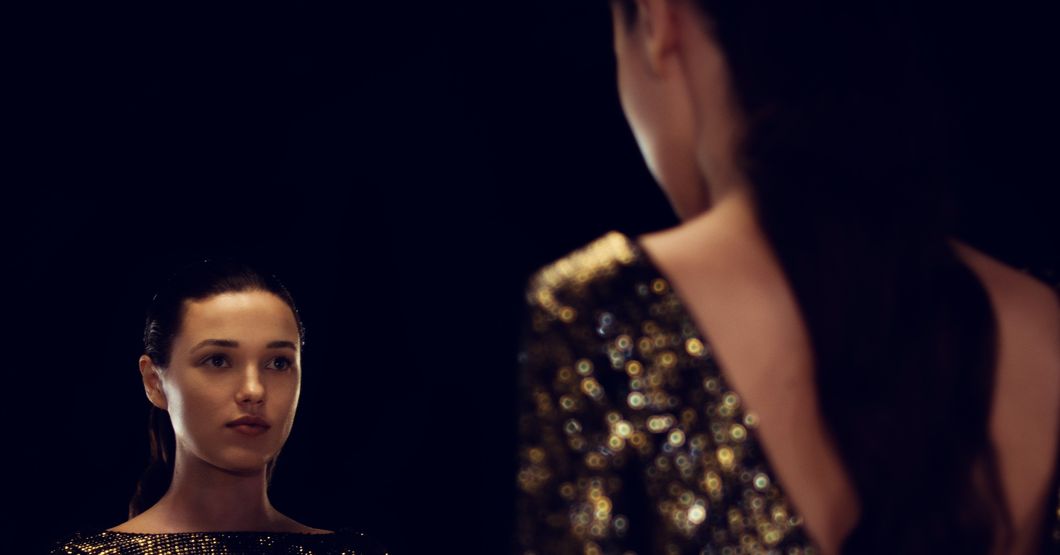 Woman  with black hair looking into a mirror in a gold dress