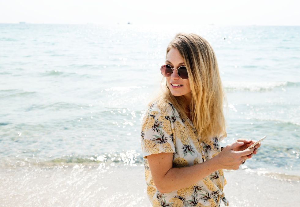 Women on beach in sunglasses posing candidly while on her cell phone