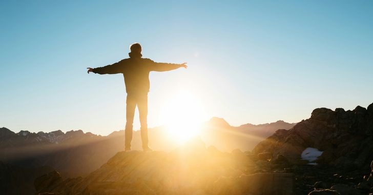 young man standing on hill embracing the sunrise filled with hope